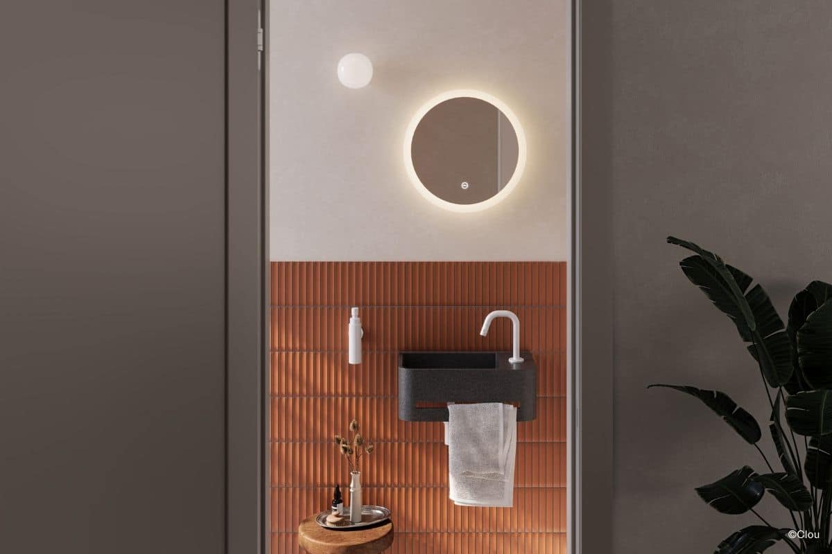 Blick in ein kleines Gäste-Wc mit halbhoch gefliester, oranger Wand, Mini-Waschtisch und Spiegel (Credit: Clou)