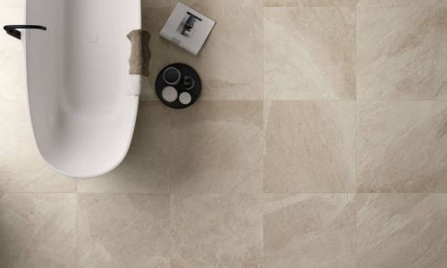 Beiges Badezimmer mit den Fliesen Shale in der Farbe Sand von Italgraniti auf dem Boden verlegt sowie eine freistehende wei&szlig;e Badewanne