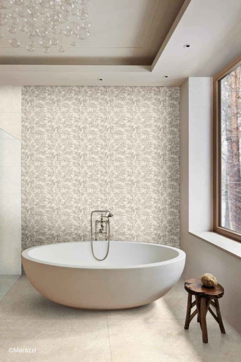 Inspirationsbild aus der Marazzi Kollektion Limestone Wall: Bereich rund um eine wei&szlig;e freistehende Badewanne mit schlichten Fliesen in Beige auf dem Boden sowie gemusterten Dekorfliesen in Beige an der Wand