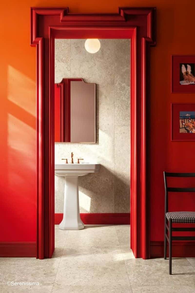 au&szlig;ergew&ouml;hnliches Bad in Beige als Inspirationsbild f&uuml;r die Serenissima Fliesen-Kollektion Grande in Falda: beige Marmoroptik an Wand und Boden, kombiniert mit knallroter Sockelleiste sowie einer knallroten Wandgestaltung im angrenzenden Raum