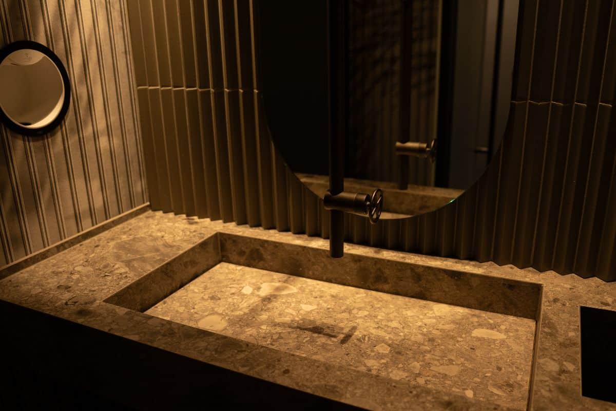 Waschtisch-Idee aus der Kr&uuml;ger Hannover Manufaktur: Waschtisch-Sonderanfertigung aus Fliesen mit einem geradlinigen Design in warmer Natursteinoptik, verstecktem Schlitzablauf, freih&auml;ngender, au&szlig;ergew&ouml;hnlicher Waschtischarmatur und eine stimmungsvollen Beleuchtung